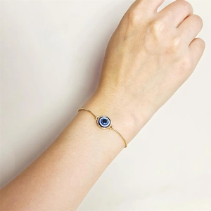 Bracelet ajustable doré œil porte-bonheur bleu sur poignet de mannequin, style épuré