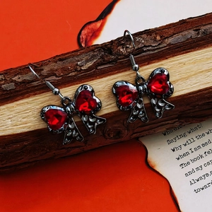 Gothic bow drop earrings with red heart crystals on rustic wood over orange backdrop