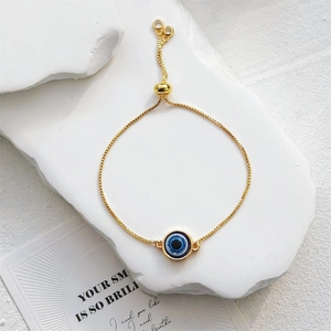 Bracelet ajustable œil grec doré avec pendentif bleu posé sur un support en pierre