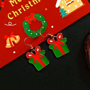 Close-up of green Christmas gift box earrings with red bows and gold enamel finish