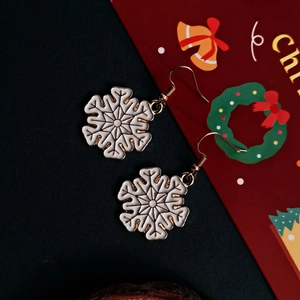 Detailed view of white enamel snowflake drop earrings with golden alloy hooks