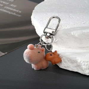 Pink flocked Capybara keychain with small brown charm and silver metal clasp on stone