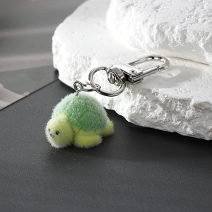 Cute green flocking turtle keychain with silver metal hook on a white textured stone