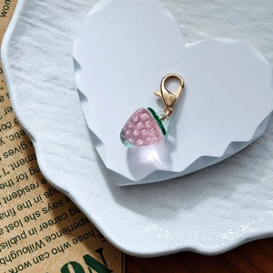 Mini pink resin strawberry charm with golden lobster clasp on a white heart tray