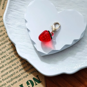 Detailed view of red resin strawberry pendant with green leaf and golden lobster clasp