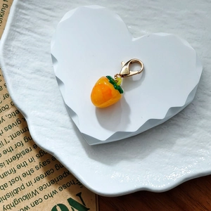Close-up of a mini yellow resin strawberry pendant with a golden lobster clasp on a stone