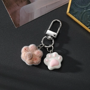 Dettaglio di zampa di gatto rosa floccata e ciondolo in resina bianca su portachiavi in metallo
