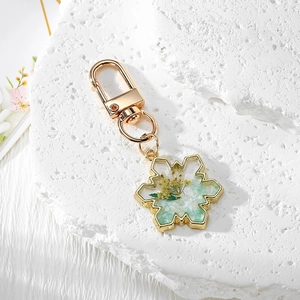 Snowflake resin keychain with real yellow dried flowers and green stones on white stone
