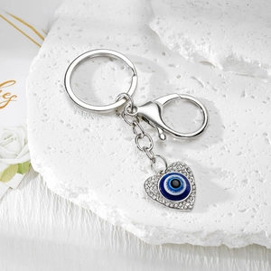 Detail of silver heart evil eye keychain with sparkling rhinestones on stone background