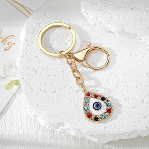 Close-up of golden teardrop evil eye keychain with rhinestones on a white stone base