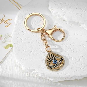 Golden Evil Eye keychain with blue teardrop pendant on a white marble display pedestal
