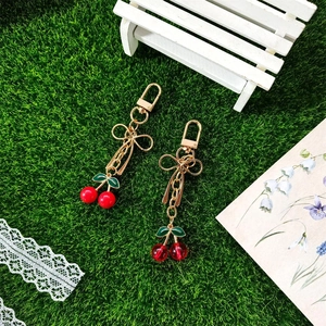 Cute cherry keychains with gold bows on grass background in a sweet pastoral style
