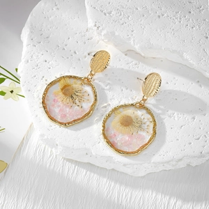Handmade resin daisy flower earrings with gold frame and dried stones on stone background