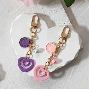 Pink and purple heart keychain pendants with gold bells and coins on a stone tray