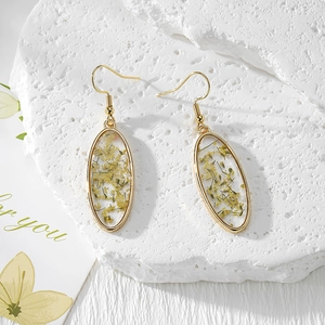 Detailed macro view of oval gold drop earrings with real yellow dried flowers in resin