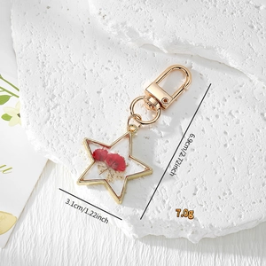 Star-shaped keychain with gold metal frame featuring red dried flowers in clear resin