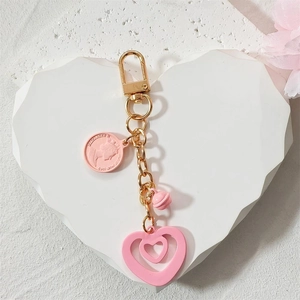 Pink heart keychain with gold bell and coin charm on a white stone base decoration