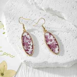 Handmade oval resin earrings with purple dried flowers and gold hooks on white stone base
