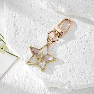 Star-shaped gold keychain with purple and white dried flowers in clear resin
