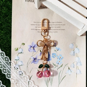 Cute gold cherry keychain with pink transparent beads and green leaf charm on vintage paper