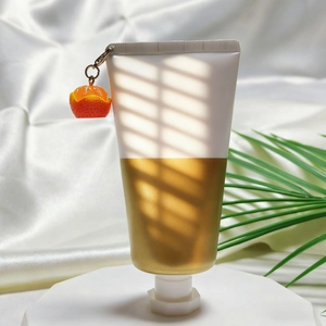 Nahaufnahme einer weiß-goldenen Kosmetiktube mit süßem Miniatur-Orangen-Fruchtanhänger