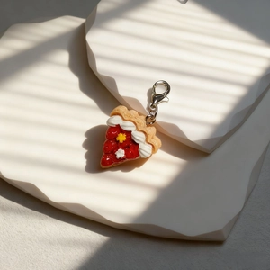 Makrodetail eines Harz-Erdbeerkuchen-Anhängers mit silbernem Karabiner auf Stein