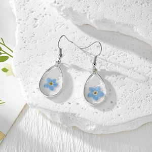 Boucles d'oreilles goutte en résine avec fleurs séchées bleues sur décor pierre