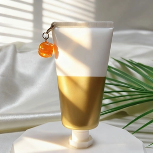 Hautpflege-Tube mit Gold-Finish und dekorativem Kürbis-Anhänger auf weißem Sockel stehend