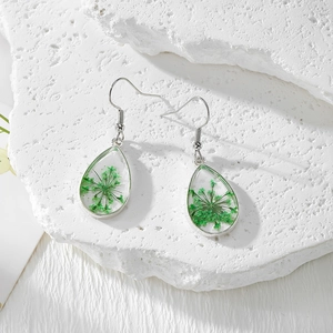 Vue détaillée de boucles d'oreilles goutte en résine avec vraies fleurs séchées vertes