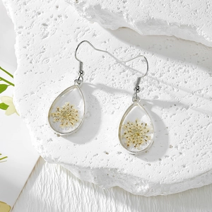 Détail de boucles d'oreilles goutte en résine avec fleurs séchées sur une base de pierre
