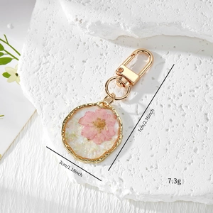Irregular resin keychain with pink dried flowers and gold metal frame on stone background