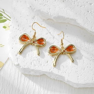 Detailed view of handmade bow earrings with orange dried flowers and golden resin frames
