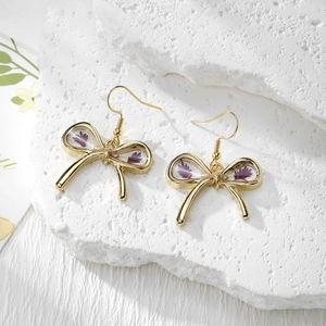 Detailed close-up of bow earrings with real purple dried flowers in resin and gold metal hooks