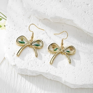 Detailed close-up of bow earrings with real white dried flowers and green leaves inlay