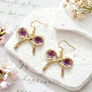 Detail of handmade resin gold bow earrings with real purple dried flowers on stone base