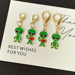 Detail of four green alien charms with red hearts and golden lobster clasps for bags