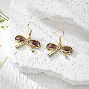 Detailed macro view of handmade bow earrings with real purple dried flowers in resin