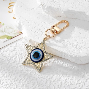Golden hexagram Evil Eye keychain with sparkling crystals on white marble stone