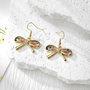 Detailed macro view of bow-shaped resin earrings with real pink dried flowers and gold hooks