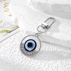 Detail of evil eye keychain with silver rhinestones and blue center on white stone