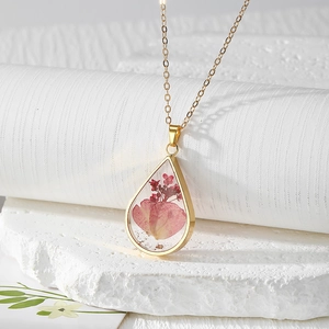 Macro detail of teardrop resin pendant with real pink flowers on gold cross chain