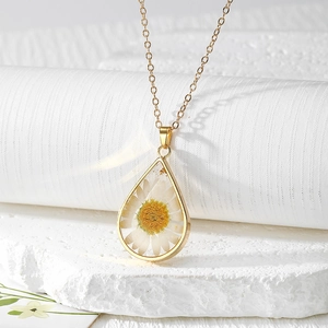 Macro shot of a teardrop resin pendant featuring a real white daisy and gold chain