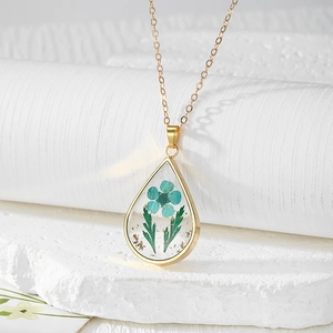 Macro shot of gold teardrop resin necklace with blue dried flowers and gold foil flakes