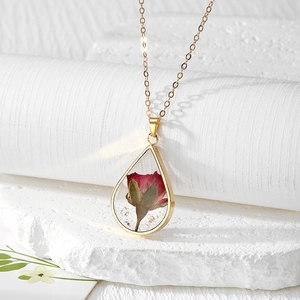 Close-up of golden teardrop pendant featuring a real red rose and gold foil flakes