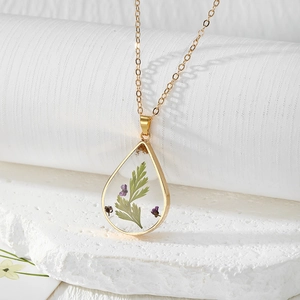 Macro detail of teardrop resin pendant with purple dried flowers on a gold chain