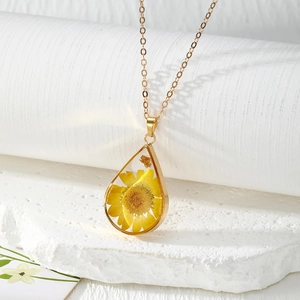 Detail of teardrop resin necklace with yellow dried daisy and gold leaf on golden chain