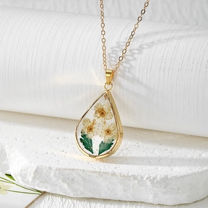 Macro detail of teardrop resin pendant with real dried flowers and gold leaf accents
