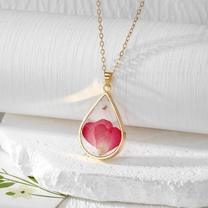 Detail of teardrop resin pendant with pink petals and gold flakes on white stone