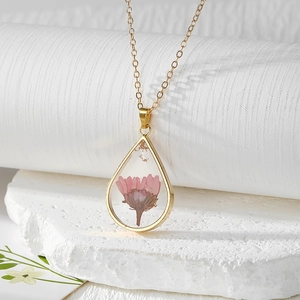 Close-up of teardrop resin pendant featuring pink dried flower and gold foil flakes