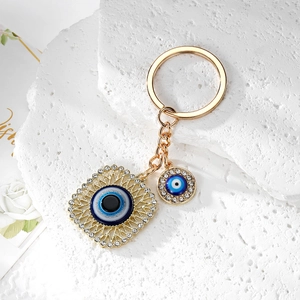 Detailed macro of golden Evil Eye keychain with sparkling crystals on a white stone background